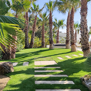 Jardin type tropical avec pelouse artificielle entre les arbres et dalles de cheminement