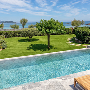 Jardin paysager avec gazon synthétique, piscine et cheminement en dalles face à la mer