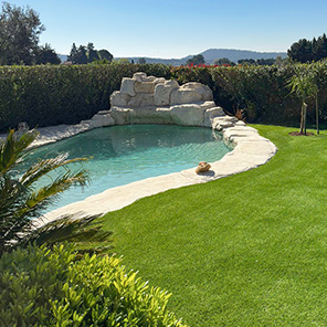 Piscine avec cascade en rochers dans un jardin en gazon artificiel
