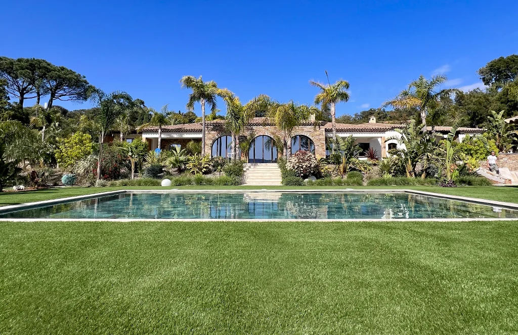 Gazon synthétique Luxe 50 posé autour d'une piscine dans jardin tropical avec palmiers