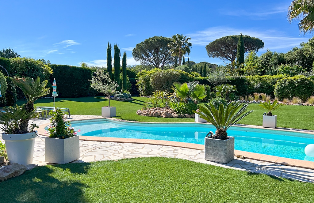Grand jardin arboré avec piscine arrondie entourée de pelouse artificielle