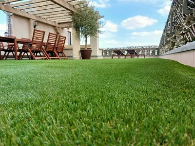 Achat et pose de gazon synthétique à Paris 1 Gros plan sur les brins du gazon synthétique, coin repas sous pergola en arrière-plan