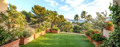 Gazon synthétique sur un balcon en bord de mer, maintenu au sol par des jardinières placées le long des bords, palmiers agités par le vent en arrière-plan